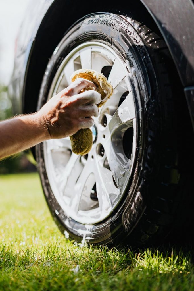 Close-up of a person washing a car tire with foam and sponge outdoors.
